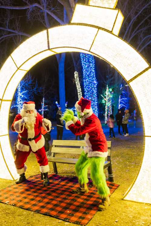 Two costumed characters, Santa and the Grinch, dance in front of a lit archway at a festive holiday event.