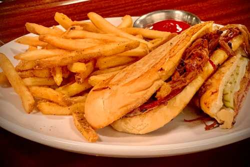 A plate of crispy French fries and two toasted sandwiches with pulled meat, served with a side of ketchup.