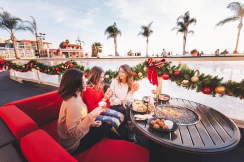 Three friends enjoy festive treats and drinks on a patio decorated for the holidays, with palm trees in the background.