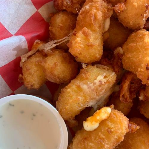 A close-up of golden fried food pieces on a red and white checkered paper, with a small cup of dipping sauce on the side.