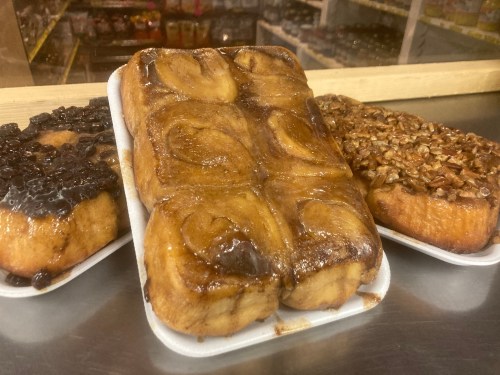 Three trays of cinnamon rolls: one with chocolate icing, one with pecans, and a classic glazed roll.