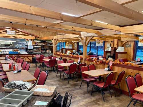 Cozy restaurant interior with wooden decor, red chairs, and tables set for dining, featuring a buffet area in the background.