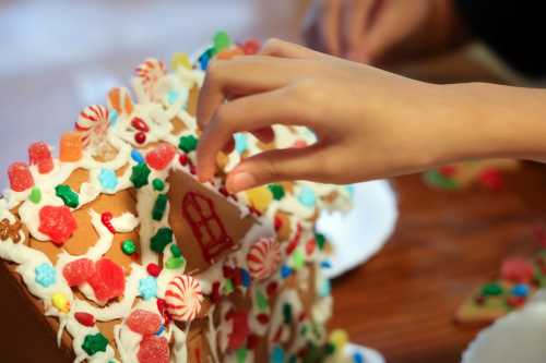 A hand decorates a gingerbread house with colorful candies and icing.