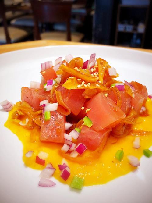 A colorful dish featuring diced watermelon, onions, and sesame seeds on a vibrant orange sauce.