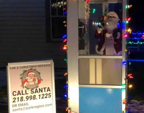 A festive phone booth with Santa inside, surrounded by colorful lights and a sign inviting calls to Santa.