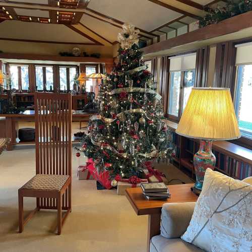 Cozy living room decorated for Christmas, featuring a large tree, a lamp, and a wooden chair.