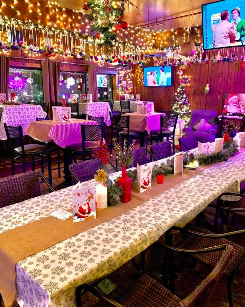 A festive dining area decorated with lights, garlands, and Christmas ornaments, featuring tables set for a celebration.