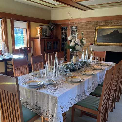 A beautifully set dining table with lace tablecloth, elegant dishes, and decorative centerpieces in a cozy room.