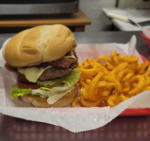 A juicy hamburger with lettuce, tomato, and cheese, served with a side of curly fries on a red tray.