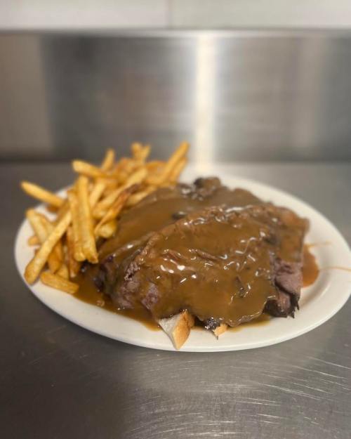 A plate of sliced beef covered in gravy, served with a side of golden French fries.