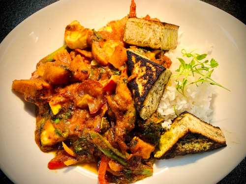 A plate of colorful vegetable curry with tofu and rice, garnished with fresh herbs.