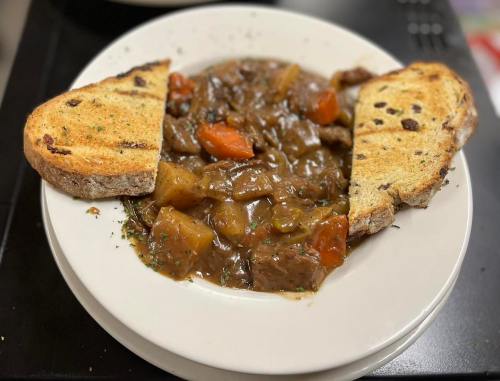 A bowl of hearty beef stew with carrots and potatoes, served with two slices of toasted bread on the side.