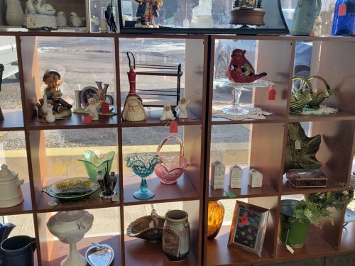 A display of various vintage items and collectibles arranged on wooden shelves in a shop window.