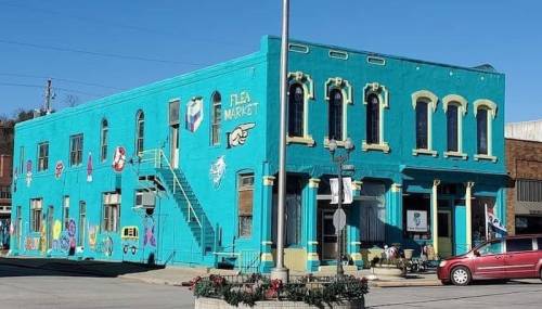 A vibrant turquoise building with colorful murals, featuring a market sign and outdoor seating area.