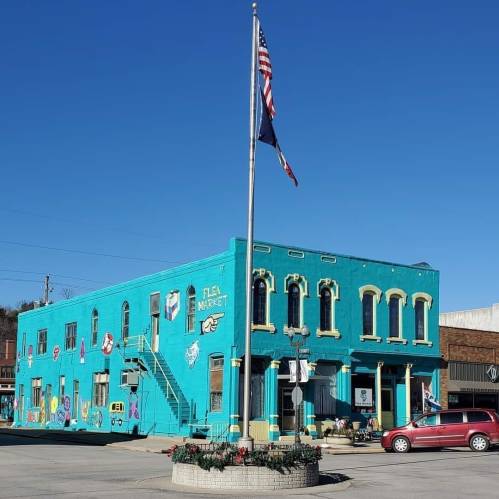 Colorful building with a mural, featuring a flagpole and a sign for a flea market, set against a bright blue sky.