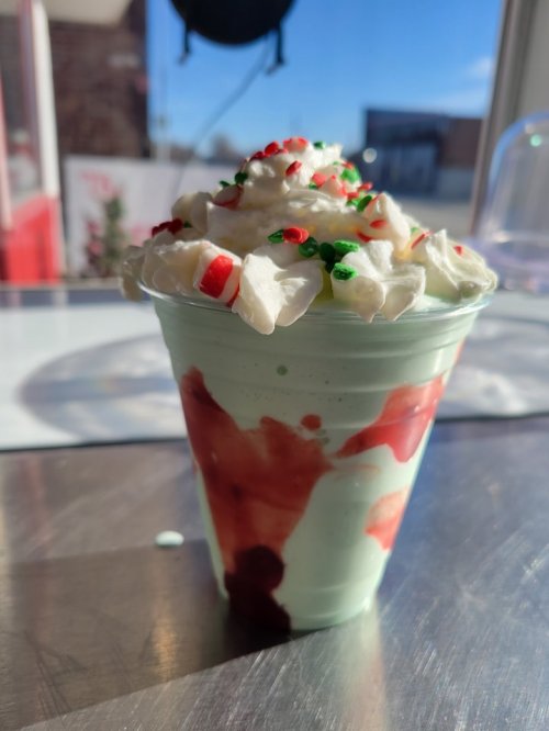 A festive mint green dessert topped with whipped cream, red and green sprinkles, and a drizzle of red sauce.