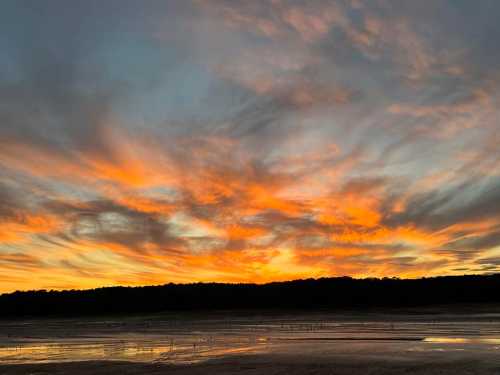 A vibrant sunset with orange and purple clouds over a calm landscape, reflecting on the water below.