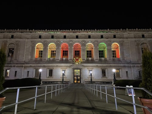 The building is illuminated with red, green, and gold lights at night, showcasing its architectural features.