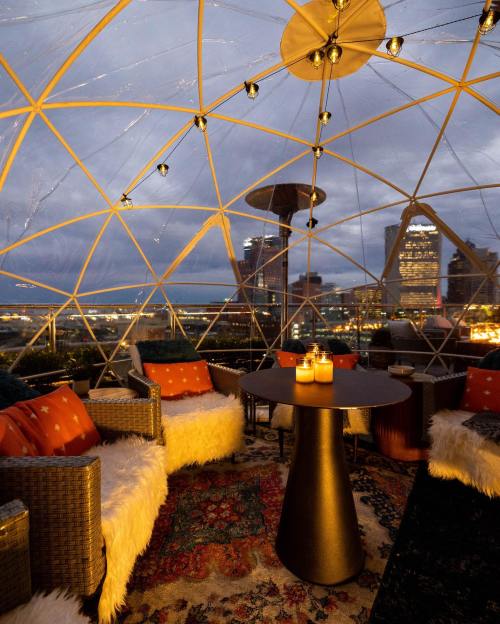 Cozy dome seating area with candles, plush cushions, and city skyline view at dusk.