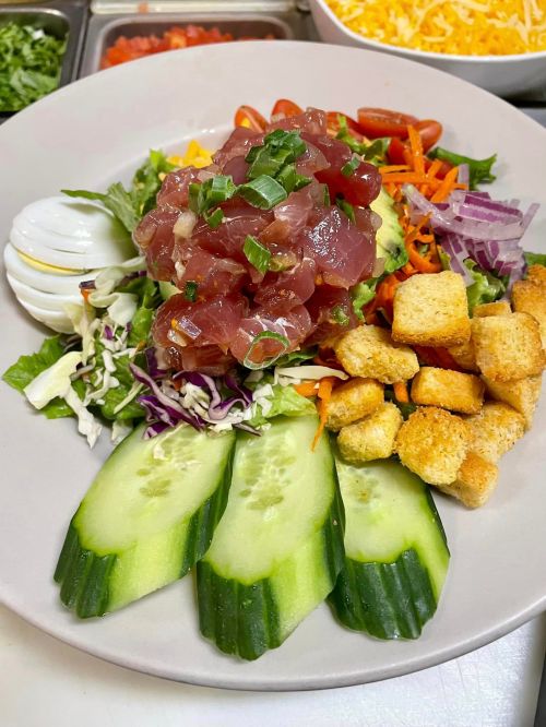 A colorful salad with tuna, mixed greens, cucumbers, croutons, and various vegetables, topped with green onions.