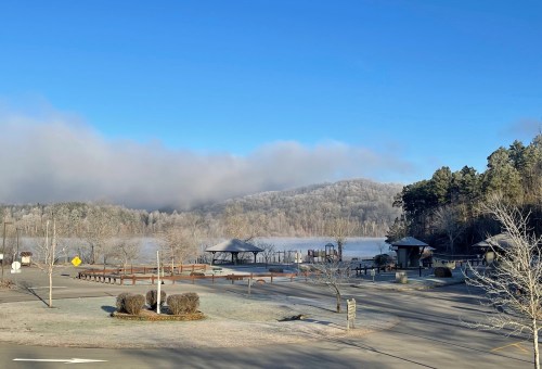 A serene winter landscape featuring a frosty lake, misty hills, and a gazebo under a clear blue sky.