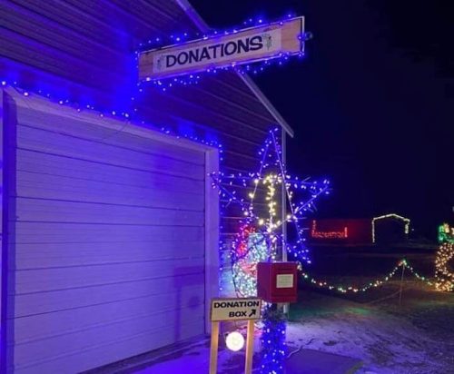 A brightly lit donation box outside a garage, decorated with colorful lights against a night sky.