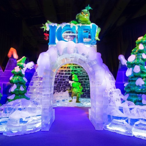 Colorful ice sculpture display featuring a whimsical archway and a character among snowy trees, illuminated with vibrant lights.
