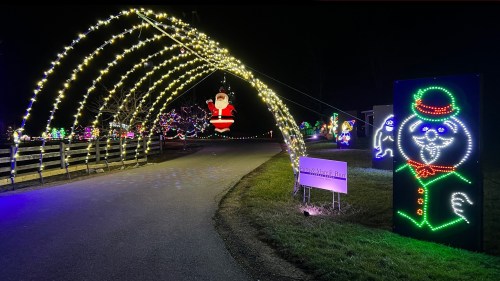 A festive pathway adorned with colorful holiday lights, featuring a Santa figure and a snowman decoration.