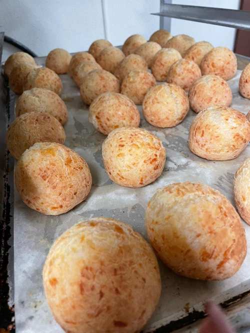A tray of golden-brown, round cheese bread balls arranged neatly on parchment paper.
