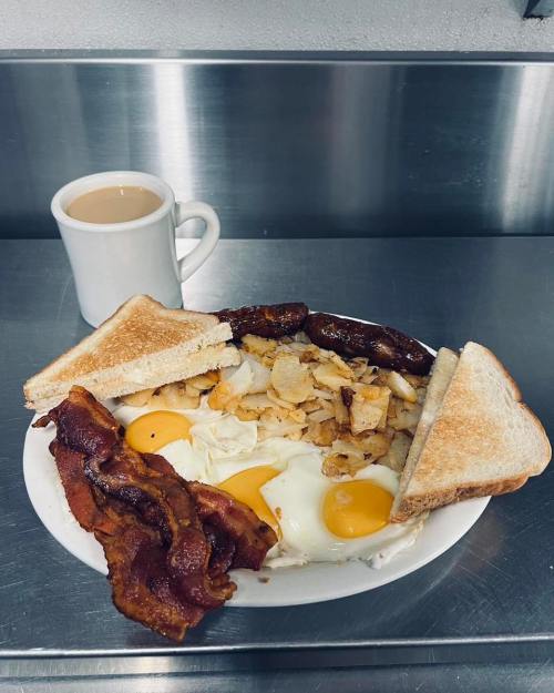 A plate of breakfast with eggs, bacon, sausage, hash browns, toast, and a cup of coffee.