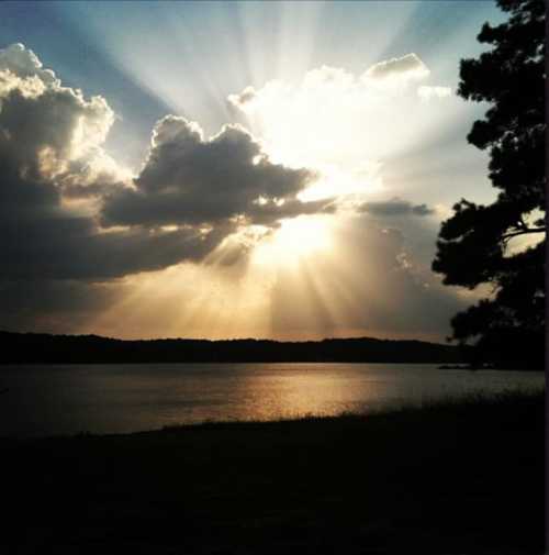 A serene lake scene at sunset, with rays of sunlight breaking through clouds and reflecting on the water.