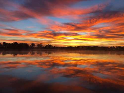 Vibrant sunset over a calm lake, with colorful clouds reflecting on the water's surface.
