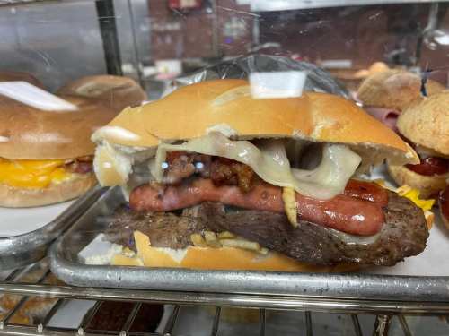A close-up of a sandwich with layers of meat, cheese, and toppings, served on a toasted bun.