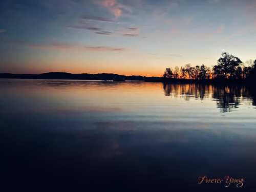 A serene lake at sunset, reflecting colorful skies and silhouetted trees along the shore.