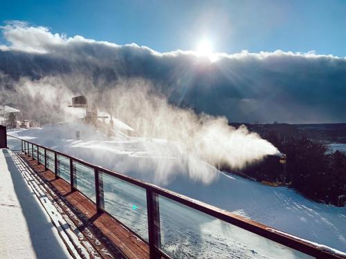 A snowy landscape with mist rising from a slope, under a bright sun and dramatic clouds in the background.