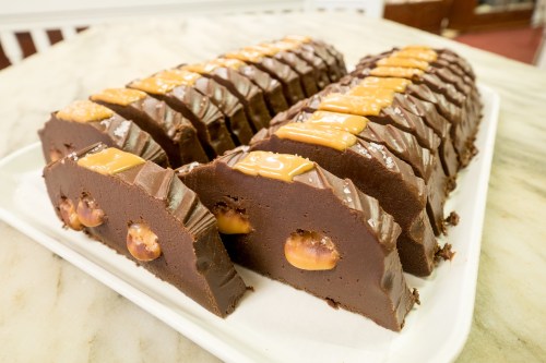 A platter of chocolate fudge slices topped with caramel and featuring whole hazelnuts inside.