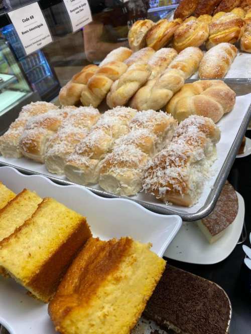 A display of assorted pastries, including coconut rolls and slices of yellow cake, arranged on trays.