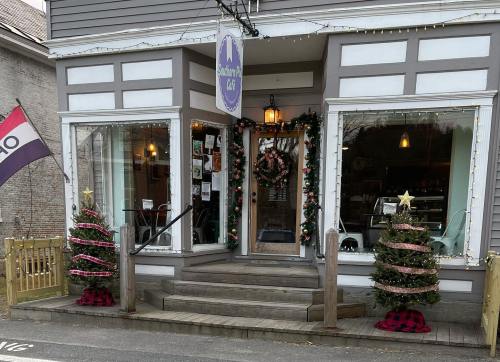 A cozy café entrance decorated for Christmas, featuring wreaths, garlands, and two festive trees with lights.