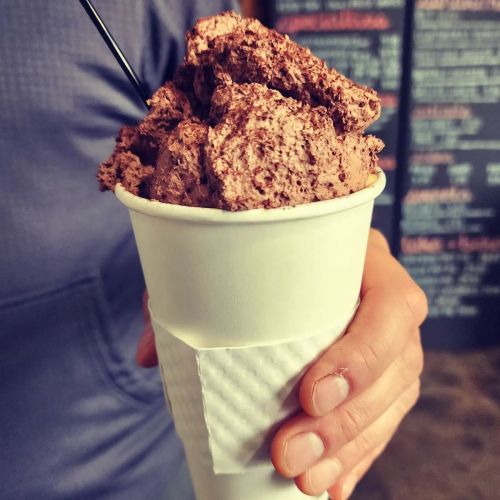 A person holding a cup filled with fluffy chocolate mousse topped with a straw.