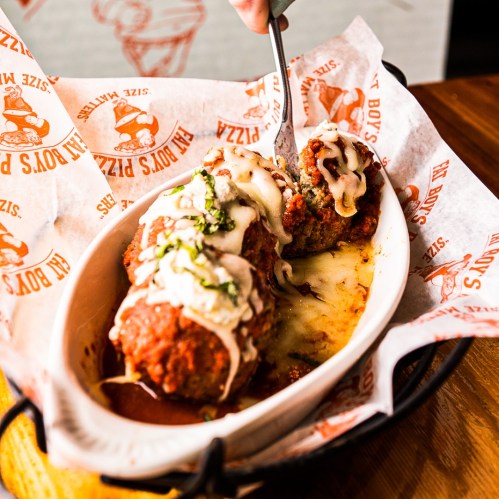 A dish of meatballs topped with cheese and sauce, served in a white bowl on a patterned paper.