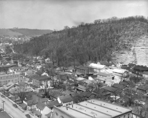 Aerial view of a small town with houses and a hillside in the background, captured in black and white.