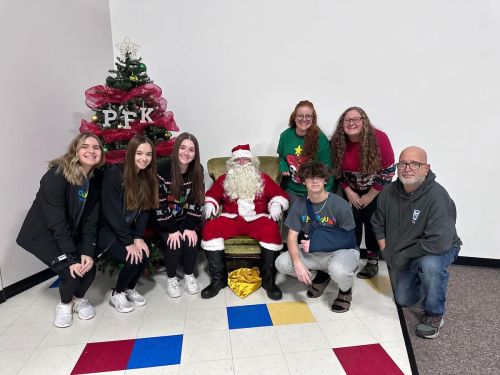 A group of seven people poses with Santa Claus in front of a Christmas tree, smiling and wearing festive attire.