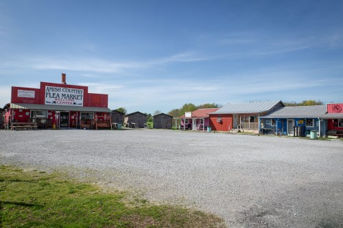 Amish Country Flea Market with colorful buildings and a gravel lot under a clear blue sky.