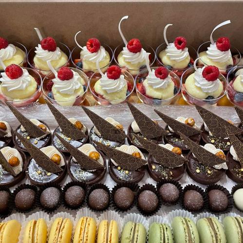 A variety of desserts including fruit cups, chocolate pastries, and colorful macarons arranged in a box.
