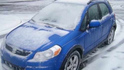 A blue car covered in snow and ice, parked on a snowy surface.