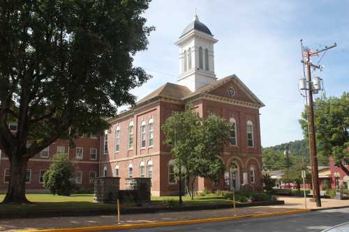 Historic brick building with a clock tower, surrounded by trees and a grassy area, under a clear blue sky.