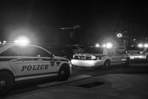 Police cars with flashing lights parked on a street at night, creating a dramatic scene in black and white.
