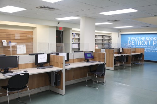 A spacious library area with computers, desks, and a blue wall featuring text about Detroit.