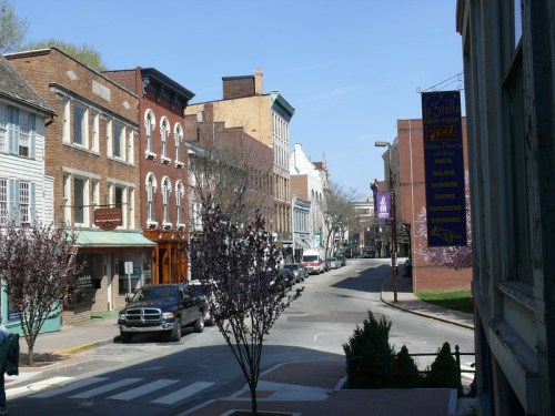 A quaint street lined with historic buildings, trees, and shops under a clear blue sky.