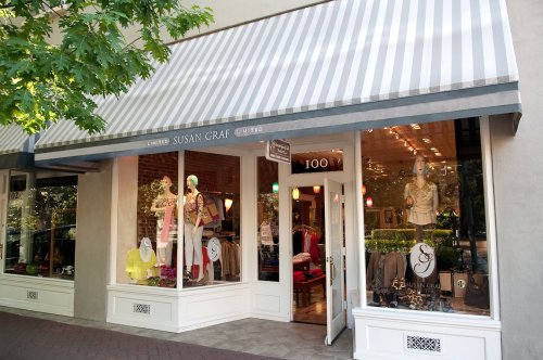A boutique storefront with a striped awning, showcasing colorful clothing and accessories in the window display.